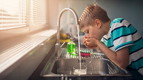 Un enfant boit de l'eau du robinet dans ses mains